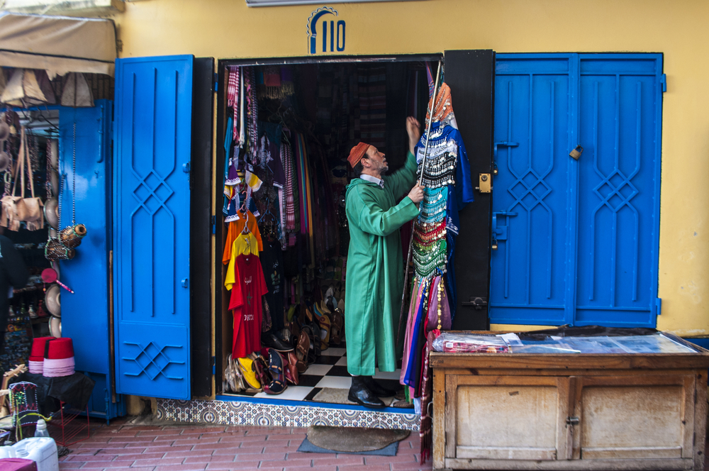 A souk vendor in front of a blue door in the Tangiers medina souk in Morocco