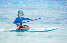 A young boy rides a surf board in blue Fijian waters