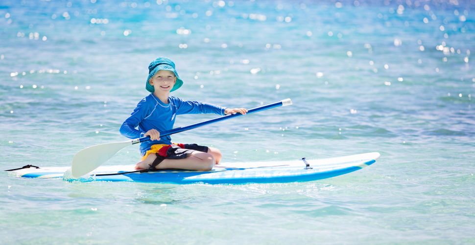 A young boy rides a surf board in blue Fijian waters