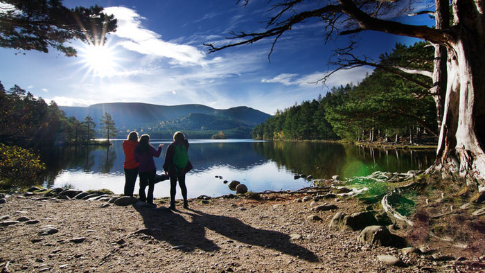 Three people standing on the peaceful shore of Loch an Eilein in Scotland