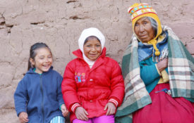 A Native Woman sits against a wall with two granddaughters