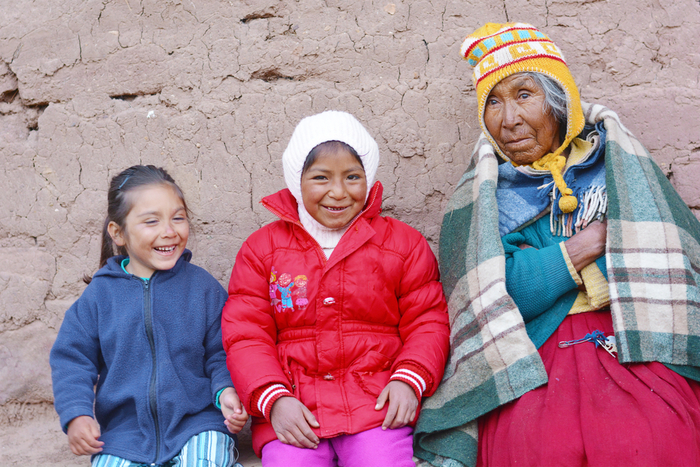 A Native Woman sits against a wall with two granddaughters